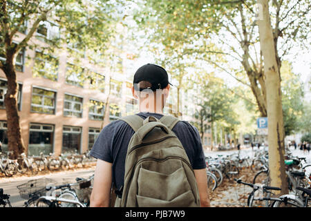 Uno studente con uno zaino o un turista su strada di Lipsia in Germania nei pressi del parcheggio per biciclette che si trova accanto alla biblioteca dell'Università di Leipig e ostello della gioventù. Foto Stock