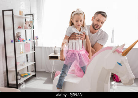 Vista frontale del padre mettendo la figlia su unicorn Foto Stock