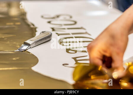 Decorazione di Natale tagliati da un lucido golden stampa. Giovane donna lavora con una precisione a mano cutter. Foto Stock