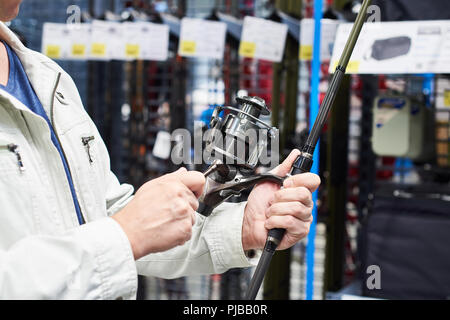 Uomo sceglie la canna da pesca nel negozio di articoli sportivi Foto Stock