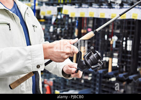 Uomo sceglie la canna da pesca nel negozio di articoli sportivi Foto Stock