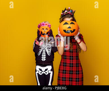 Colorato halloween. moderna la madre e il bambino in stile messicano costume di halloween isolato su sfondo giallo azienda jack-o-lantern zucche nella parte anteriore Foto Stock