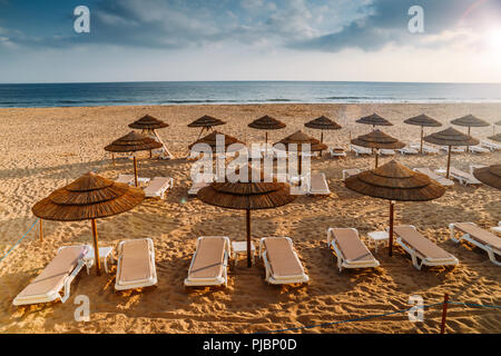 La paglia ombrelloni e sdraio sulla spiaggia sabbiosa di di Carcavelos beach a Lisbona, Portogallo Foto Stock