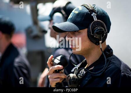 Oceano Pacifico (16 luglio 2018) Specialista del personale marittimo Oscar Lopez, da South Bend, Ind. ascolta per informazioni da varie stazioni di guardare come le visite-missile destroyer USS Dewey (DDG 105) conduce a una ricostituzione in mare. Dewey è in corso negli Stati Uniti La terza area della flotta di operazioni. Foto Stock