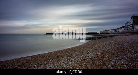 Il sole tramonta dietro il molo e la spiaggia a Hastings nel Canale della Manica costa del Sussex. Foto Stock