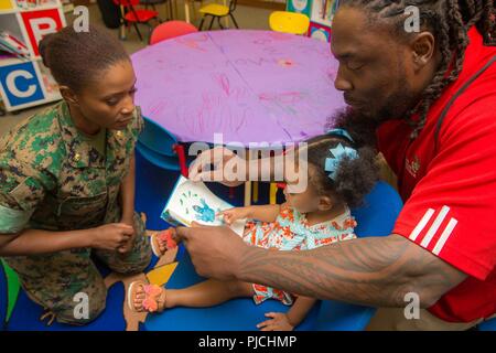 Ricky Jean Francois, un tackle difensivo giocatore di calcio nella National Football League, legge un libro a sua nipote all'interno del Marine Corps Biblioteca Universitaria, Marine Corps base Quantico, Virginia, luglio 19, 2018. Il sig. Jean Francois era touring la base con sua sorella, U.S. Marine Corps Il Mag. Villiana Jean Francois, fornitura officer, 4 Marine Logistics Group, per contribuire a promuovere le risorse umane e gli affari di riserva Behavioral Salute e prevenzione dei suicidi Programma. Foto Stock