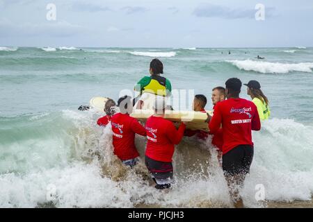 Stati Uniti Marines con il 3° Reggimento Marine aiutare un guerriero ferito ottenere attraverso il surf durante il guerriero ferito giorno alla bianca spiaggia Plaines, Kapolei, Hawaii, lug. 18, 2018. L'evento ha fornito sia active duty e il veterano combattenti feriti la possibilità di godersi il mare per il giorno.. Foto Stock