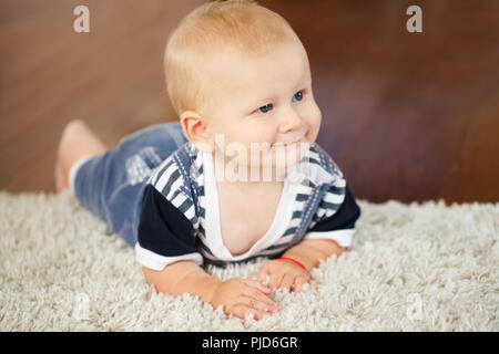 Ritratto di carino adorabile bionda sorridente caucasica baby boy con gli occhi blu sdraiato sul pavimento in kids bambini camera che guarda lontano Foto Stock