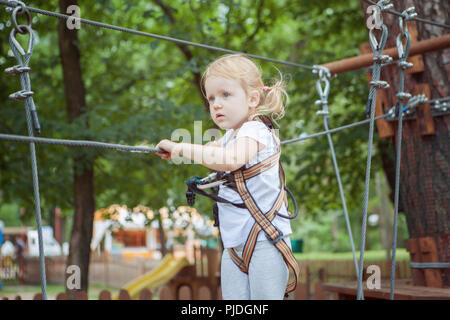 Ritratto di una coraggiosa bambina in corda park. Lei passa l'ostacolo. Foto Stock