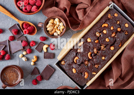 Close-up di cioccolato fondente ciambellone dal glutine di farina di grano saraceno con dadi e lamponi in un metallo stampo da forno su una tabella di calcestruzzo con tazza o Foto Stock