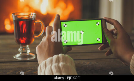 Primo piano immagine della donna tenendo lo smartphone e fare foto di firepalce a casa. Svuotare lo schermo verde per inserire la propria immagine o testo Foto Stock