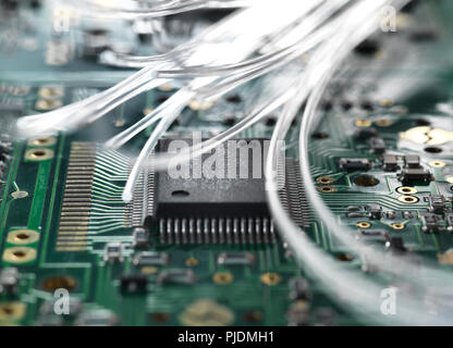 La fibra ottica che trasporta i dati passando attraverso una scheda di circuito per illustrare l'intelligenza artificiale Foto Stock