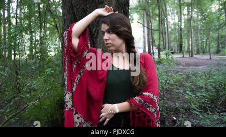Giovani hippie bella bruna donna con lunga treccia capelli vicino ad un albero riflessivo e di pensiero Foto Stock