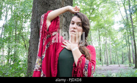 Giovani hippie bella bruna donna con lunga treccia capelli vicino ad un albero riflessivo e di pensiero Foto Stock
