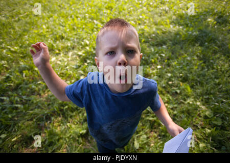 Carino bambino caucasico riproduzione di aeroplano di carta nel parco all'aperto in estate giornata di sole Foto Stock