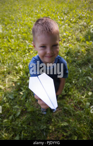 Carino bambino caucasico riproduzione di aeroplano di carta nel parco all'aperto in estate giornata di sole Foto Stock