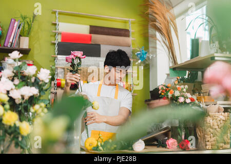 Small business. Fioraio maschio rendendo bouquet di rose al banco escursioni nel negozio di fiori. L'uomo assistant o il proprietario in floral design studio, effettuare decorazioni un Foto Stock