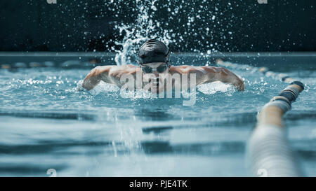 La dinamica e montare il nuotatore nel cappuccio la respirazione di eseguire la corsa a farfalla in piscina. Il giovane uomo. La fitsport, nuotatore, piscina, sano stile di vita, la concorrenza, la formazione, l'atleta, concetto energetico Foto Stock