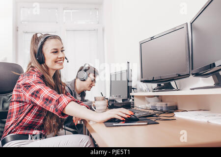 Ritratto di giovane donna sorridente con uso della cuffia con il collega di sesso maschile a computer scrivania in ufficio Foto Stock