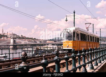 Budapest, Ungheria. Un tram giallo che corre lungo il Fiume Danubio sul lato Pest con il ponte di Szechenyi visibile in background Foto Stock