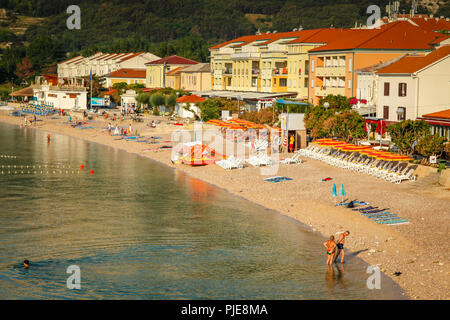 Le persone godono la piccola spiaggia presso l'hotel rivestito seaside resort villaggio di Baska sull'isola croata di Krk nel mare Adriatico Foto Stock