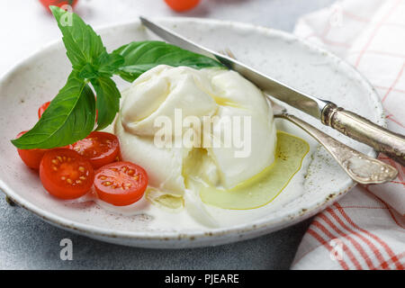 Deliziosi piatti della cucina italiana fresco formaggio burrata con pomodorini e pesto di basilico e olio di oliva in una piastra bianca. Snack Gourmet. Messa a fuoco selettiva Foto Stock