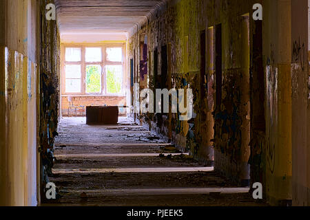 Grungy corridoio in un edificio abbandonato con luce proveniente dalle camere a destra. Alla fine di una sedia e un battuto sopra la scrivania può essere visto. Foto Stock