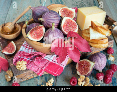 Fichi maturi in una ciotola di legno, rosso lampone, zucchero di canna, miele e un tovagliolo a scacchi sulla vecchia scheda di taglio come pure le foglie di autunno giacciono sul vecchio woode Foto Stock