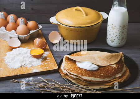 Fresca, frittelle di caldo in una padella, le uova, il latte, la farina su un tavolo di legno. Foto Stock