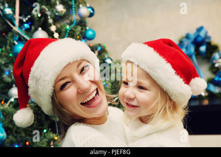 Madre e figlia in santa hat vicino albero di Natale Foto Stock