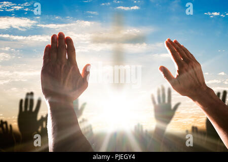 Mano umana alzando le mani con la croce al centro contro il cielo nuvoloso Foto Stock