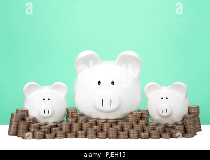 Salvadanaio di tre banche in fila uno grande con due piccole dietro un muro di monete accatastati in pile. Parete di risparmio. Segni di dollaro nei loro occhi. Luce verde backg Foto Stock