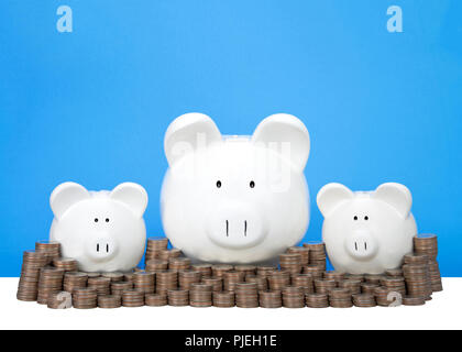 Salvadanaio di tre banche in fila uno grande con due piccole dietro un muro di monete accatastati in pile. Parete di risparmio. Segni di dollaro nei loro occhi. Sfondo blu w Foto Stock