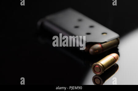 Solo proiettile con una pistola di clip in background isolata su uno sfondo nero. Caricatore di pistola caricato completamente. Commerciante di armi. Foto Stock