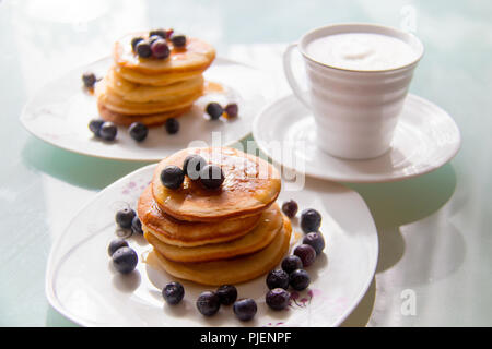 La colazione frittelle sul piatto elegante servita con mirtilli freschi e guarnita con originale di sciroppo di acero, prossima Coppa del bianco crema caffè Foto Stock