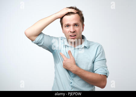 Giovane Uomo in camicia blu con il sudore trail su di esso. Egli è la sudorazione becaise di temperatura calda in ufficio. Foto Stock