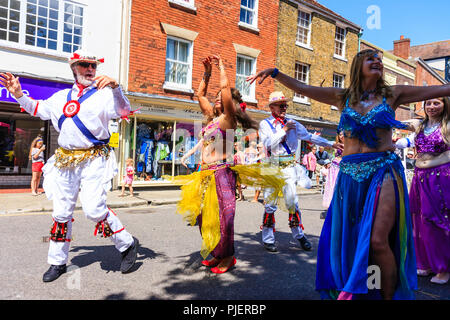 Donne mature da "buon karma Ladies' danza del ventre gruppo eseguire con alcuni enti locali Morris ballerini in una strada della città di Sandwich Kent. Foto Stock