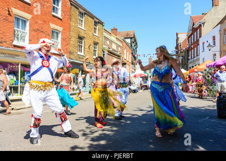 Donne mature da "buon karma Ladies' danza del ventre gruppo eseguire con alcuni enti locali Morris ballerini in una strada della città di Sandwich Kent. Foto Stock