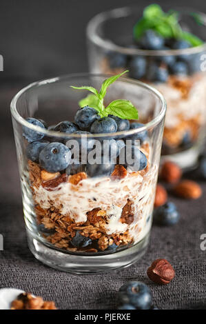 Home muesli fatto colazione con mirtilli e yogurt, servita in bicchieri su uno sfondo grigio Foto Stock