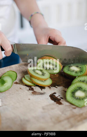 Close up di mani femminili per affettare i kiwi su un legno tagliere Foto Stock