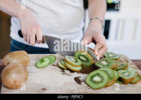 Fette di kiwi siede su un tagliere con le mani di una donna per affettare Foto Stock