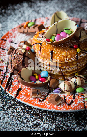 Una pila di cucinato al momento American toffee frittelle una spruzzata di sciroppo al cioccolato e guarnita con dimezzato di uova di cioccolato, dolci cioccolatini all'ora Foto Stock