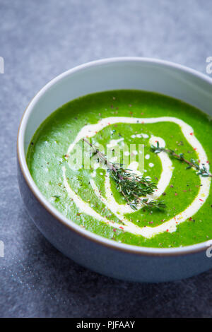 Colore verde brillante di crescione zuppa con una pioggerellina di doppia panna, guarnita con fresco rametti di timo e una macinatina di pepe e sale, su sfondo grigio Foto Stock