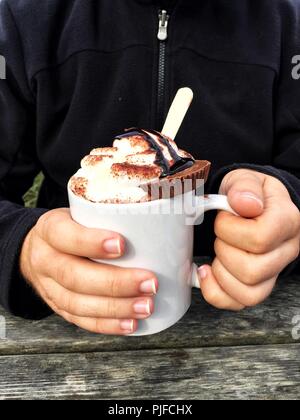 Una sezione mediana di un maschio tenendo una tazza di indulgente di cioccolata calda con panna montata e cookie sulla parte superiore Foto Stock