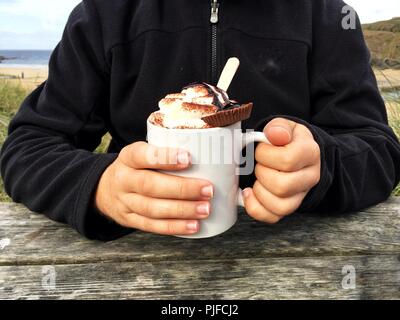 Una sezione mediana di un maschio tenendo una tazza di indulgente di cioccolata calda con panna montata e cookie sulla parte superiore Foto Stock