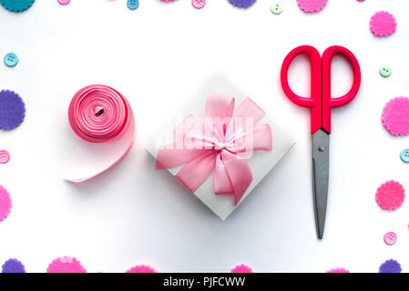 Coriandoli colorati confezione regalo fiocco di raso nastro forbici su uno sfondo bianco. Vista superiore laici piatta Foto Stock