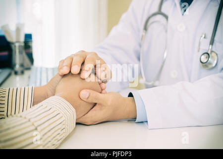 Gentile uomo medico mani tenendo la mano del paziente seduto alla scrivania di incoraggiamento, empatia, tifo e supporto durante la visita medica. Bad nuovo Foto Stock