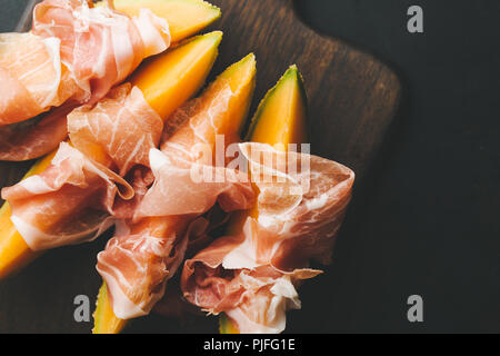 Spagnolo gustosi cibi tradizionali - antipasti mediterranea Melone e prosciutto a bordo su sfondo scuro. Primo piano. Orizzontale con copia spazio. Foto Stock