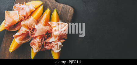 Spagnolo gustosi cibi tradizionali - antipasti mediterranea Melone e prosciutto a bordo su sfondo scuro. Primo piano. Orizzontale con copia spazio. Foto Stock