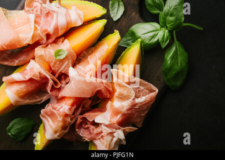 Spagnolo gustosi cibi tradizionali - antipasti mediterranea con Melone e prosciutto a bordo su sfondo scuro. Primo piano. Orizzontale con copia spazio. Foto Stock